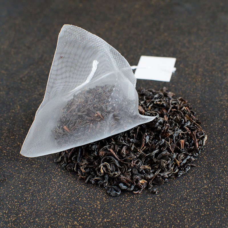 A pyramid sachet of black tea rests on a black and gold surface