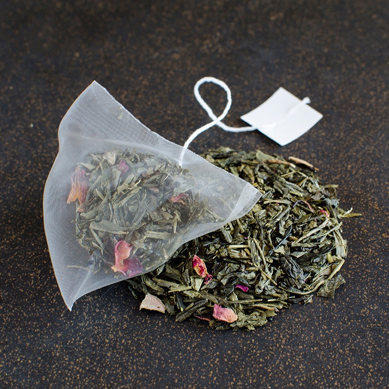 A pyramid sachet of green tea rests on a black and gold surface