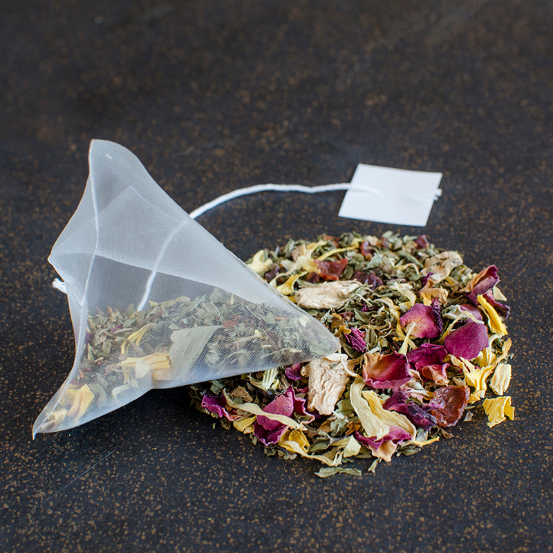A pyramid sachet of herbal tea rests on a black and gold surface