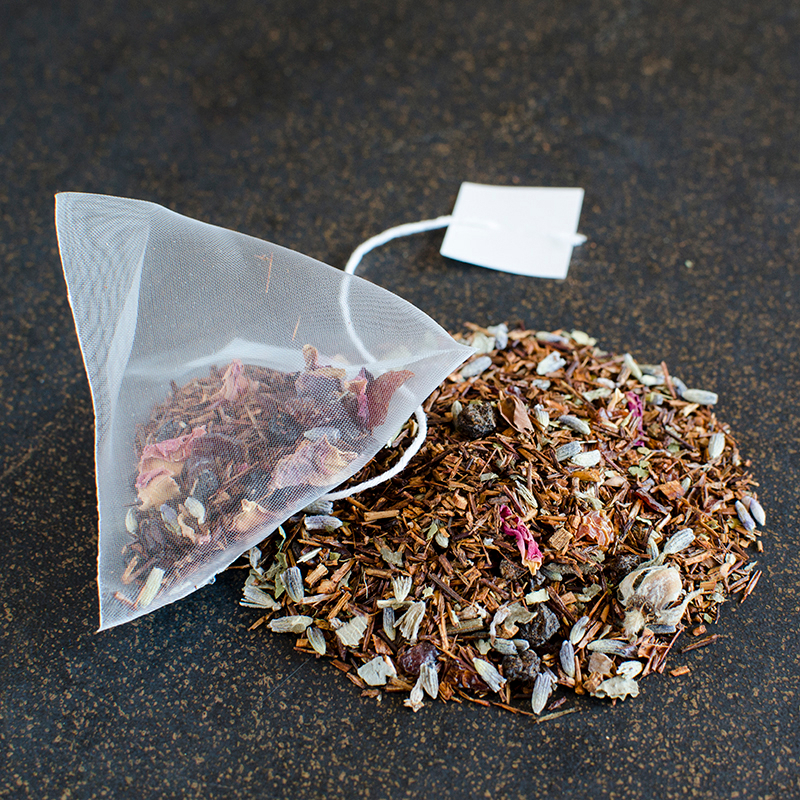 A pyramid sachet of rooibos tea rests on a black and gold surface