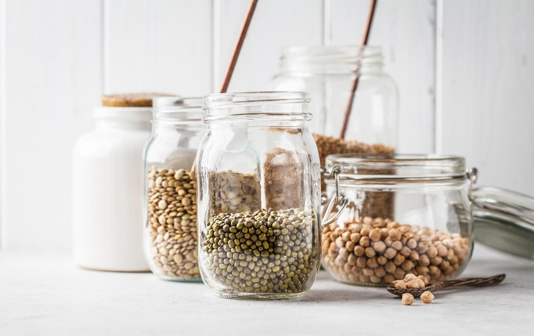 An image showing dried goods including peas and garbanzo beans in glass jars.